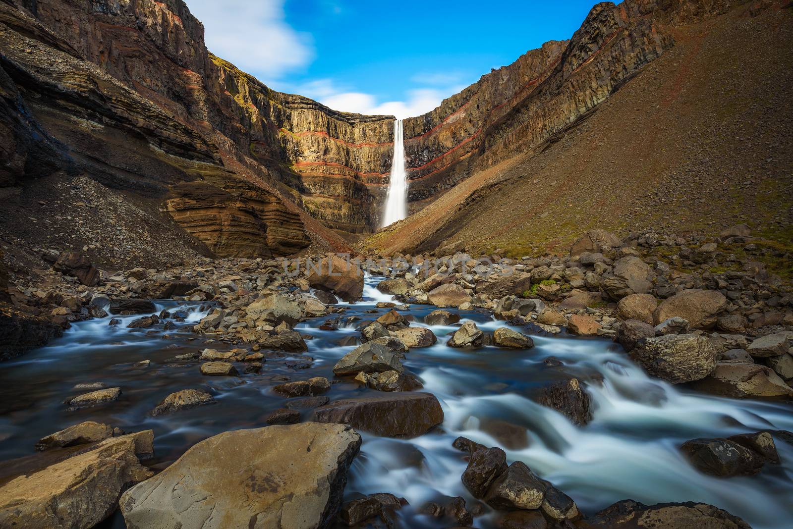 Hengifoss waterfall in East Iceland. Hengifoss is the third highest waterfall in Iceland and is surrounded by basaltic strata with red layers of clay between the basaltic layers. Long exposure.