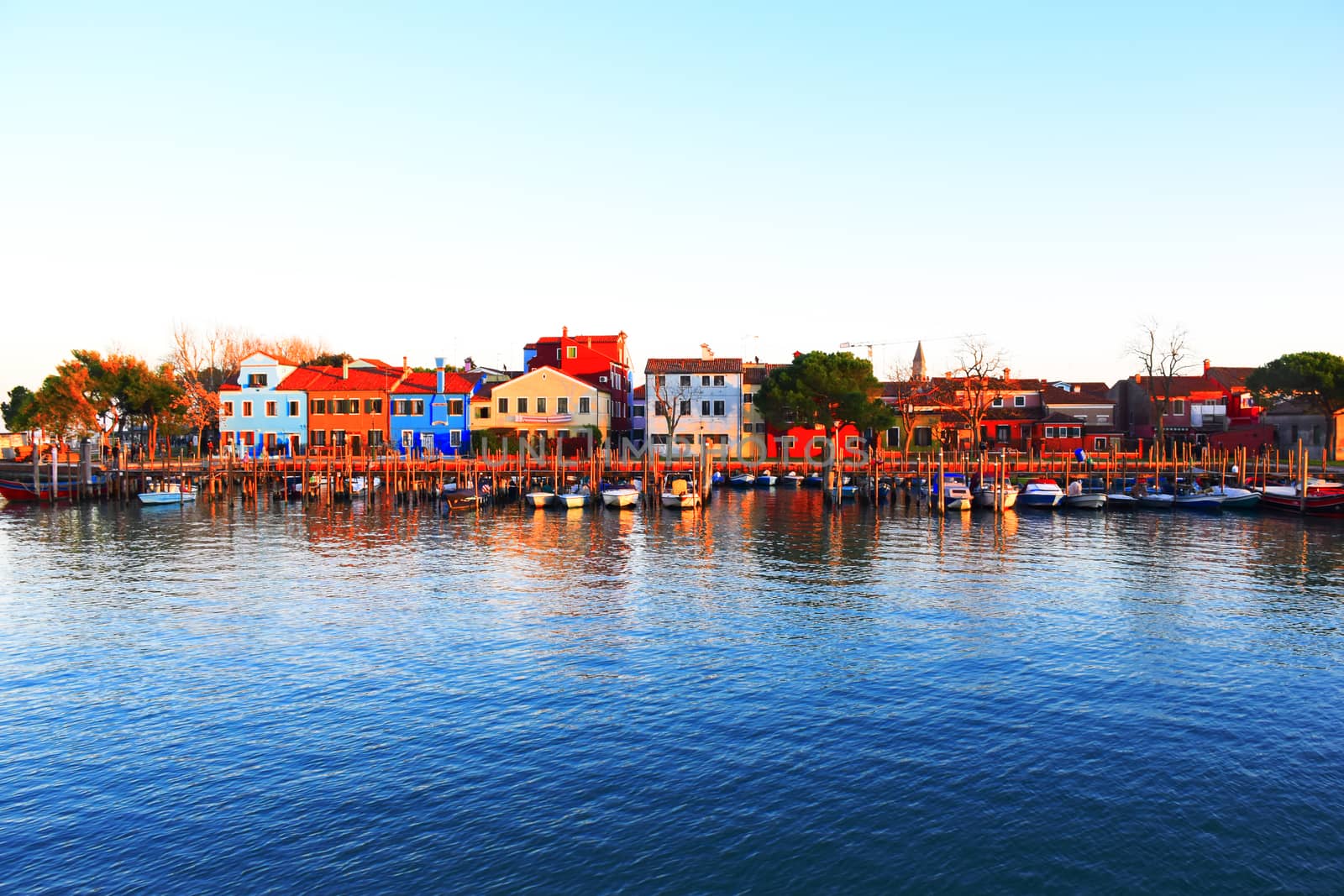 The colorful village of Burano, with its characteristic leaning bell tower, is reflected in the waters of the Venetian lagoon.