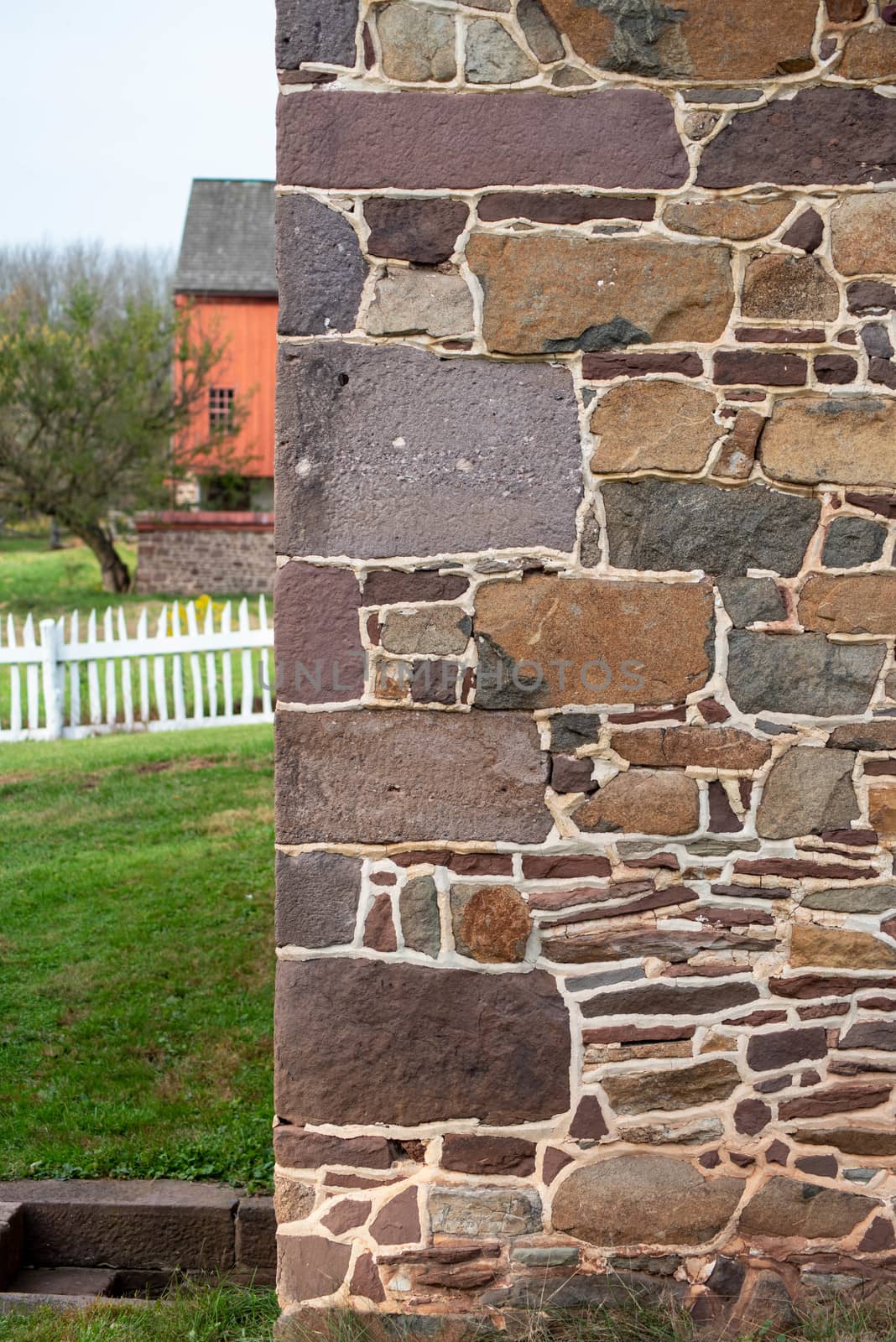 Beautiful farm scene with green grass and picket fence. Stone house cornerstones corner stones in foreground with copy space.