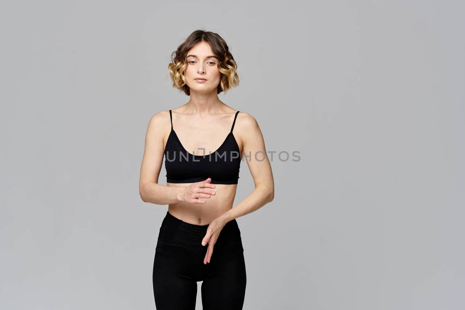 A slender woman is gesturing with her hands on a gray background Sport Fitness figure. High quality photo