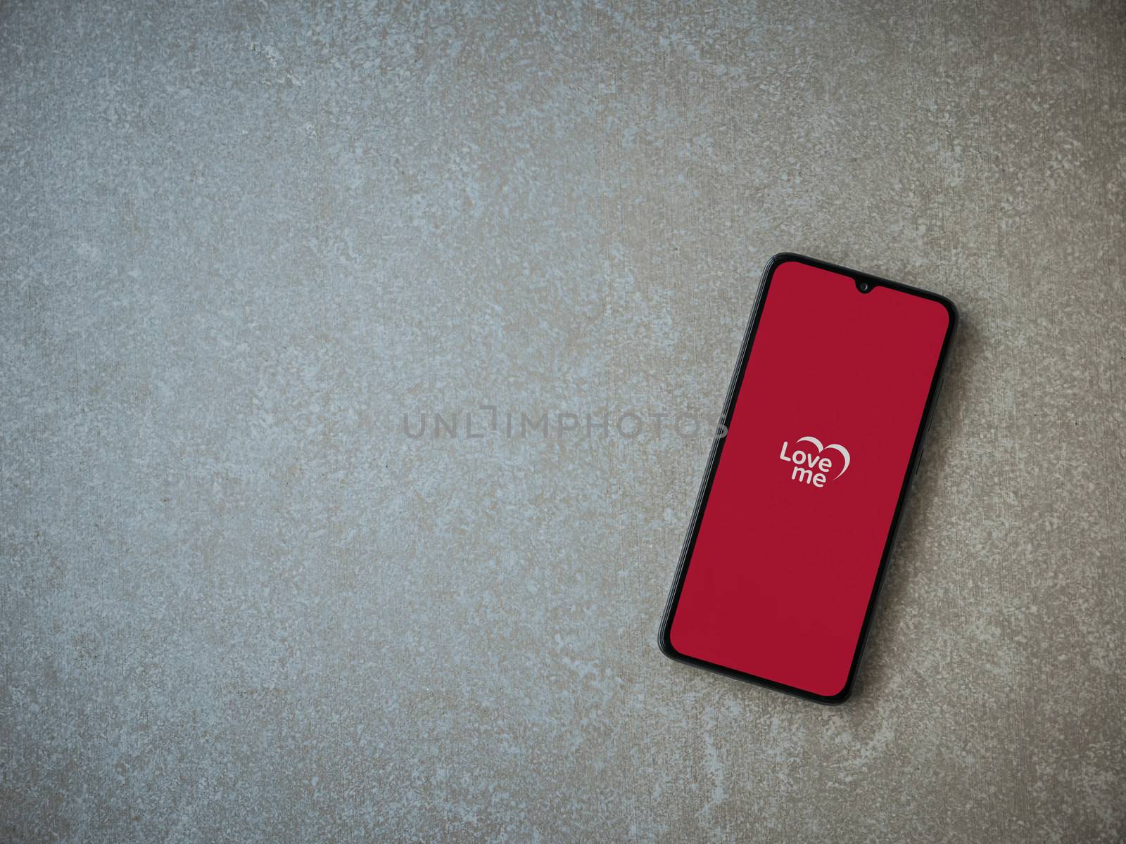 Lod, Israel - July 8, 2020: Loveme app launch screen with logo on the display of a black mobile smartphone on ceramic stone background. Top view flat lay with copy space.