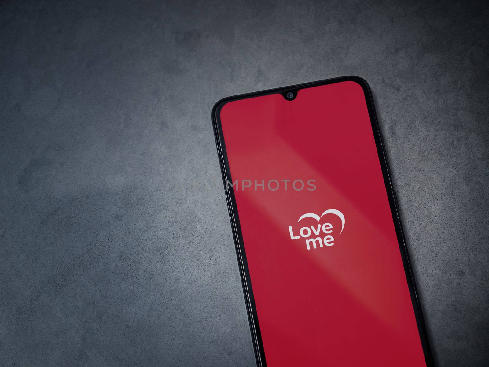 Lod, Israel - July 8, 2020: Loveme app launch screen with logo on the display of a black mobile smartphone on dark marble stone background. Top view flat lay with copy space.