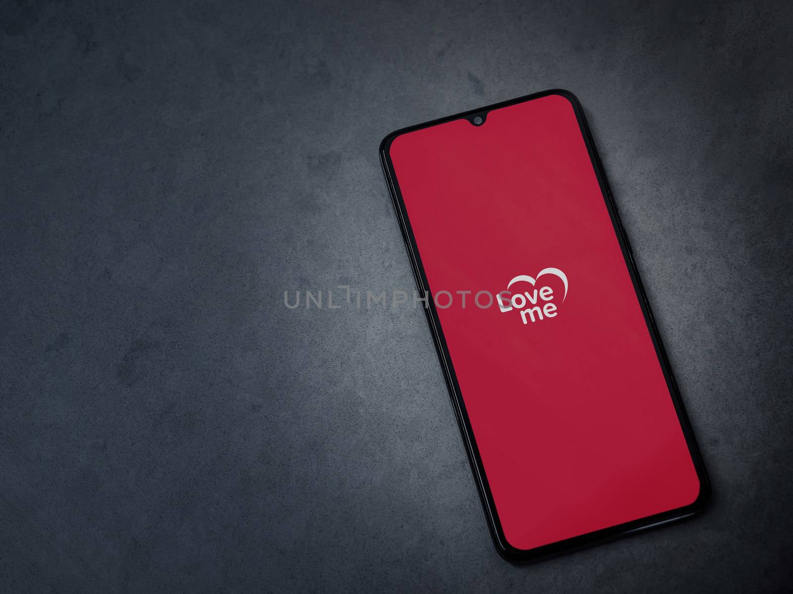 Lod, Israel - July 8, 2020: Loveme app launch screen with logo on the display of a black mobile smartphone on dark marble stone background. Top view flat lay with copy space.