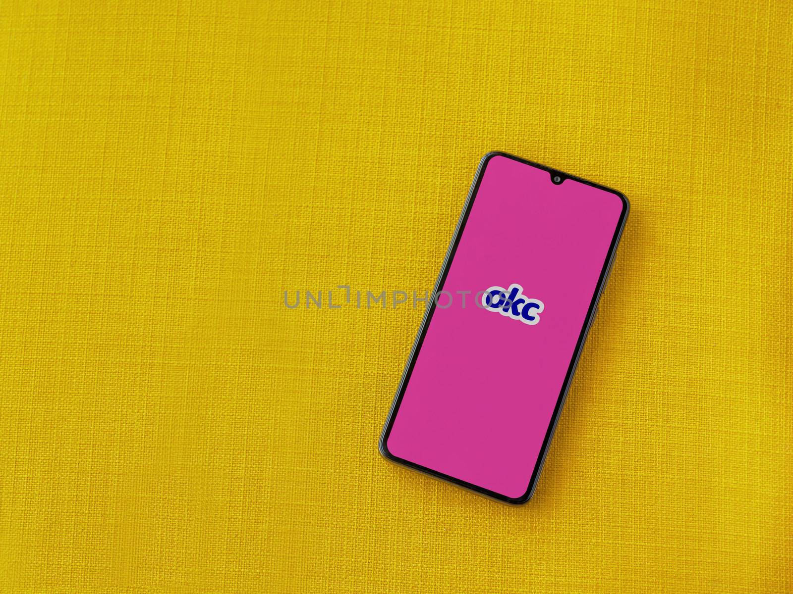 Lod, Israel - July 8, 2020: OkCupid app launch screen with logo on the display of a black mobile smartphone on a yellow fabric background. Top view flat lay with copy space.