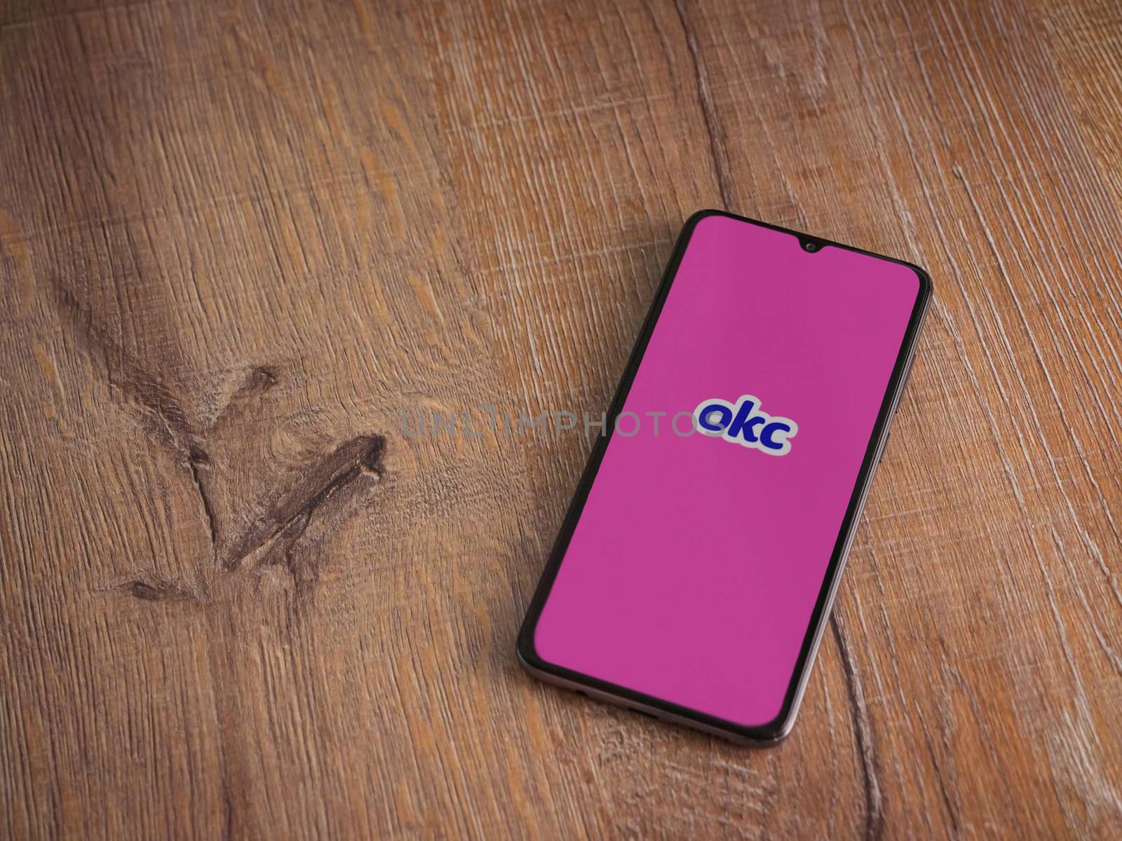 Lod, Israel - July 8, 2020: OkCupid app launch screen with logo on the display of a black mobile smartphone on wooden background. Top view flat lay with copy space.