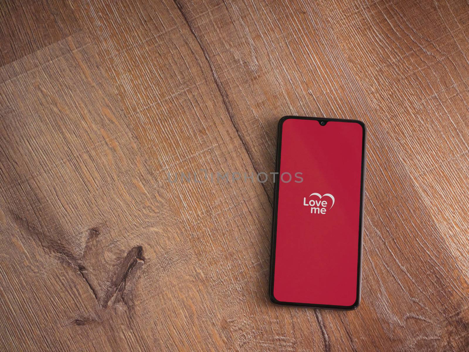 Lod, Israel - July 8, 2020: Loveme app launch screen with logo on the display of a black mobile smartphone on wooden background. Top view flat lay with copy space.