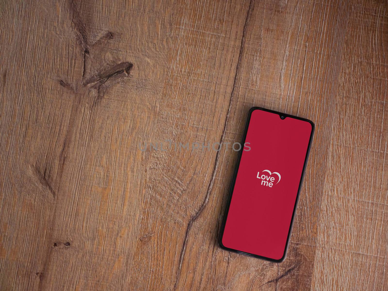 Lod, Israel - July 8, 2020: Loveme app launch screen with logo on the display of a black mobile smartphone on wooden background. Top view flat lay with copy space.