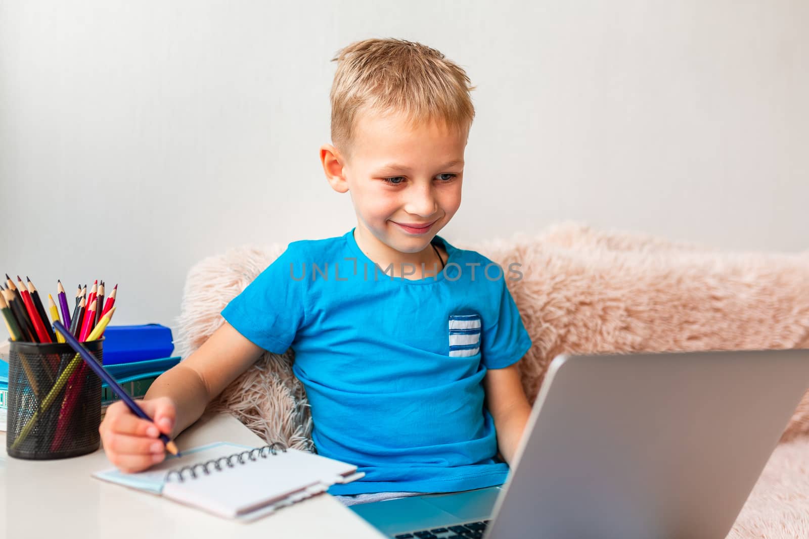 Little young school boy working at home with a laptop and class notes studying in a virtual class. Distance education and learning, e-learning, online learning concept during quarantine