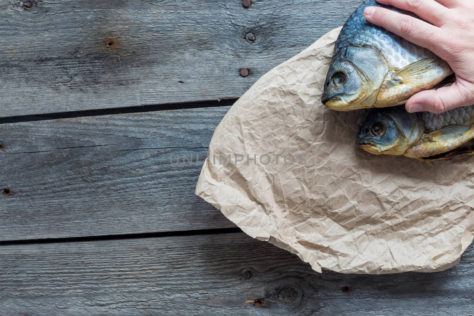 Hand holds Dried Volga bream vobla in a crumpled kraft paper roll, delicious beer snack, close-up.