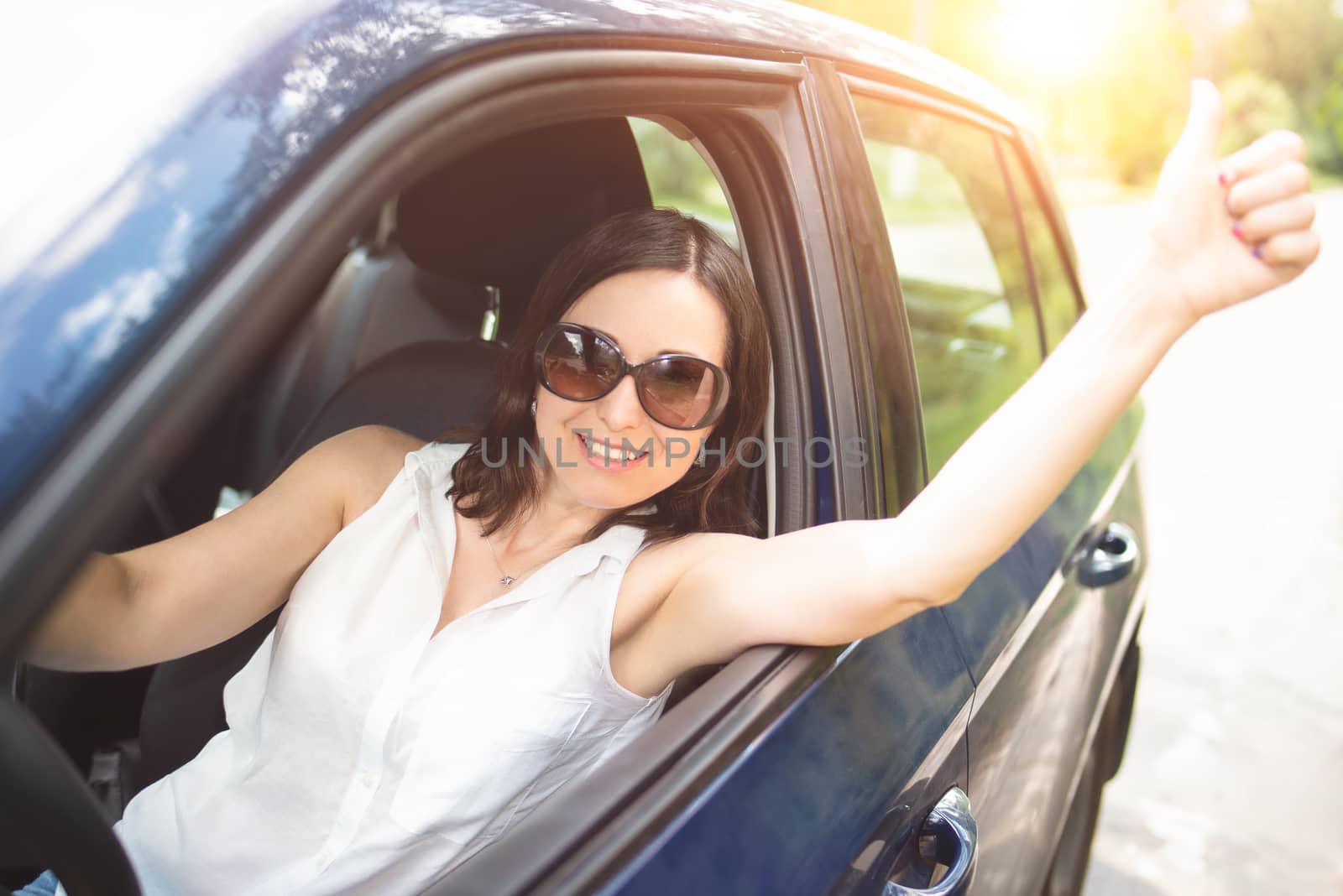 A smart looking middle-aged adult woman wearing sunglasses put her hand out the car window and raised her thumbs up.