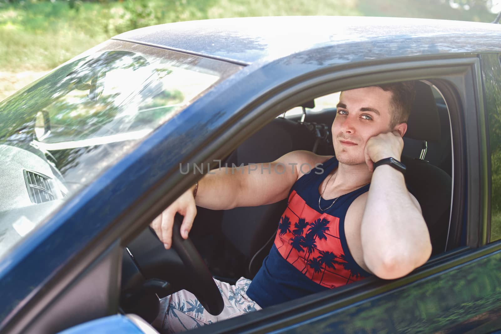 portrait of smiling young man sitting in a car and looking at the camera on a sunny day