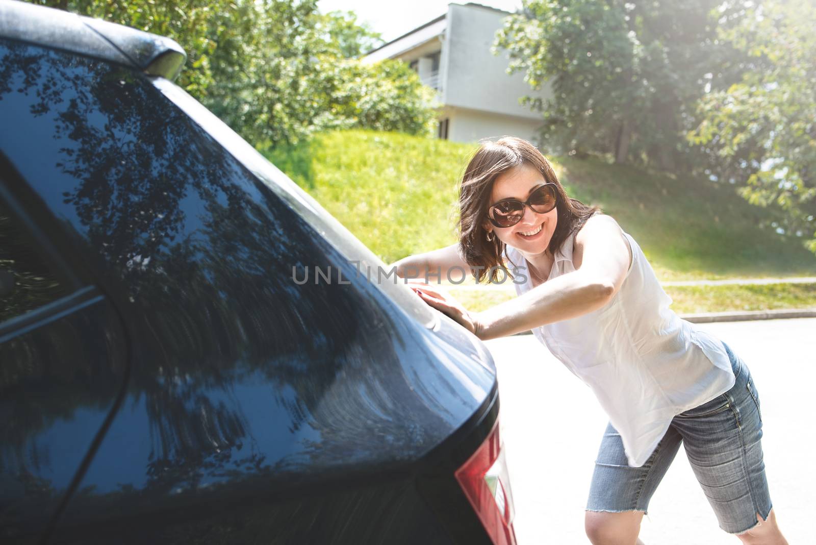 woman pushing broken car while her boyfriend is driving