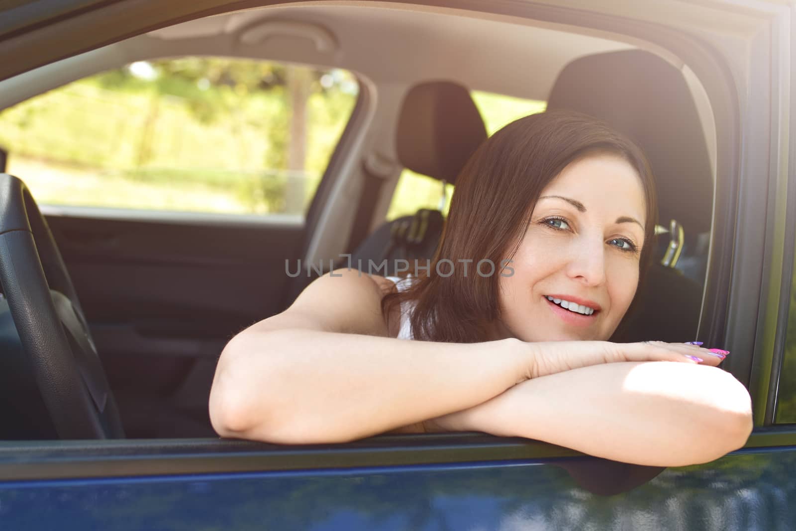 Smiling female driver looking out the car. a portrait of a smiling woman sitting in the car, looking at the camera.