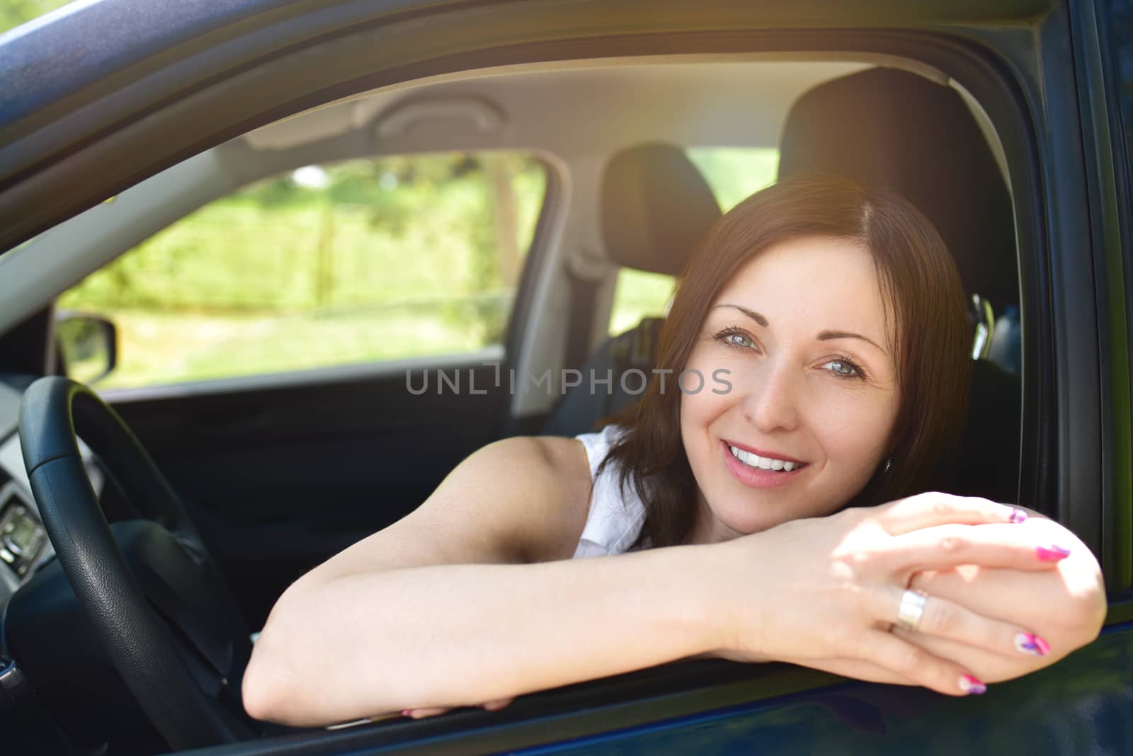 Smiling female driver looking out the car. a portrait of a smiling woman sitting in the car, looking at the camera.