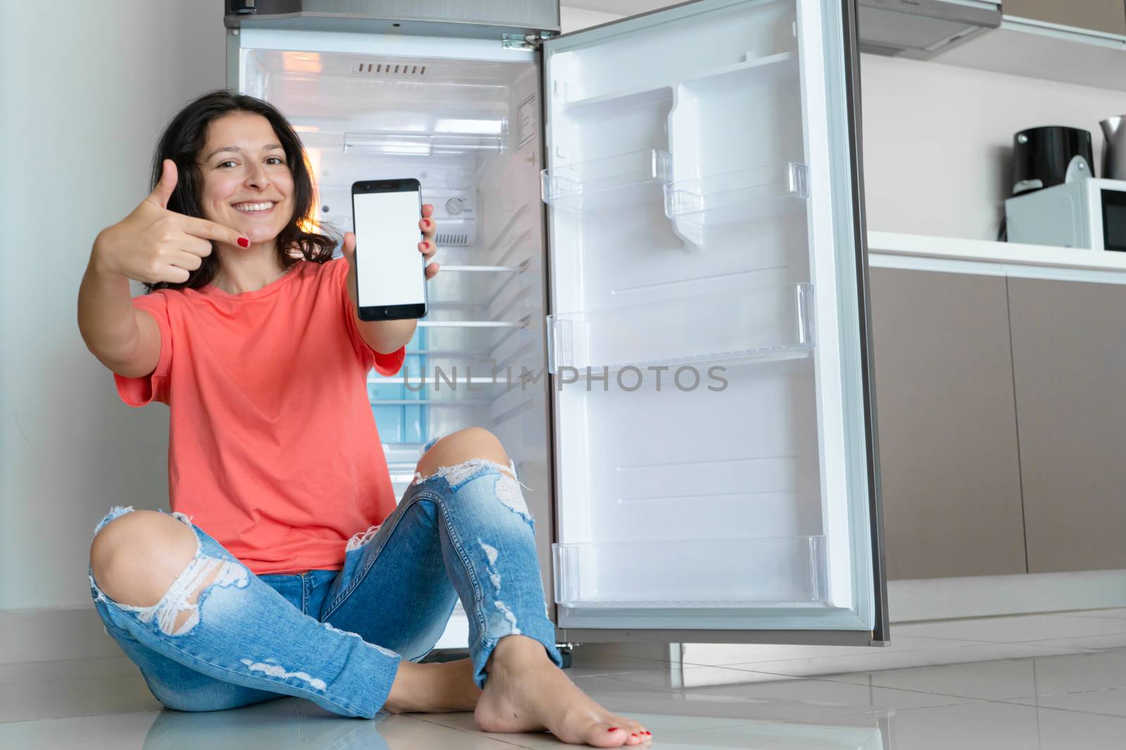 A girl orders food using a smartphone. Empty refrigerator with no food. Food delivery service advertisement.