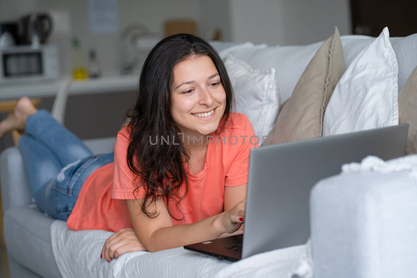 Girl lying on the couch rejoices looking at the laptop. Smiles, good mood, emotion of joy.