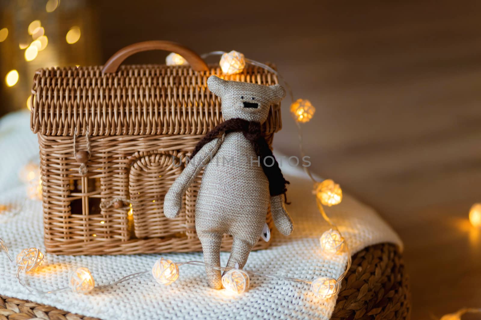 Teddy bear toy on the background of a wicker house made of rattan among Christmas garlands