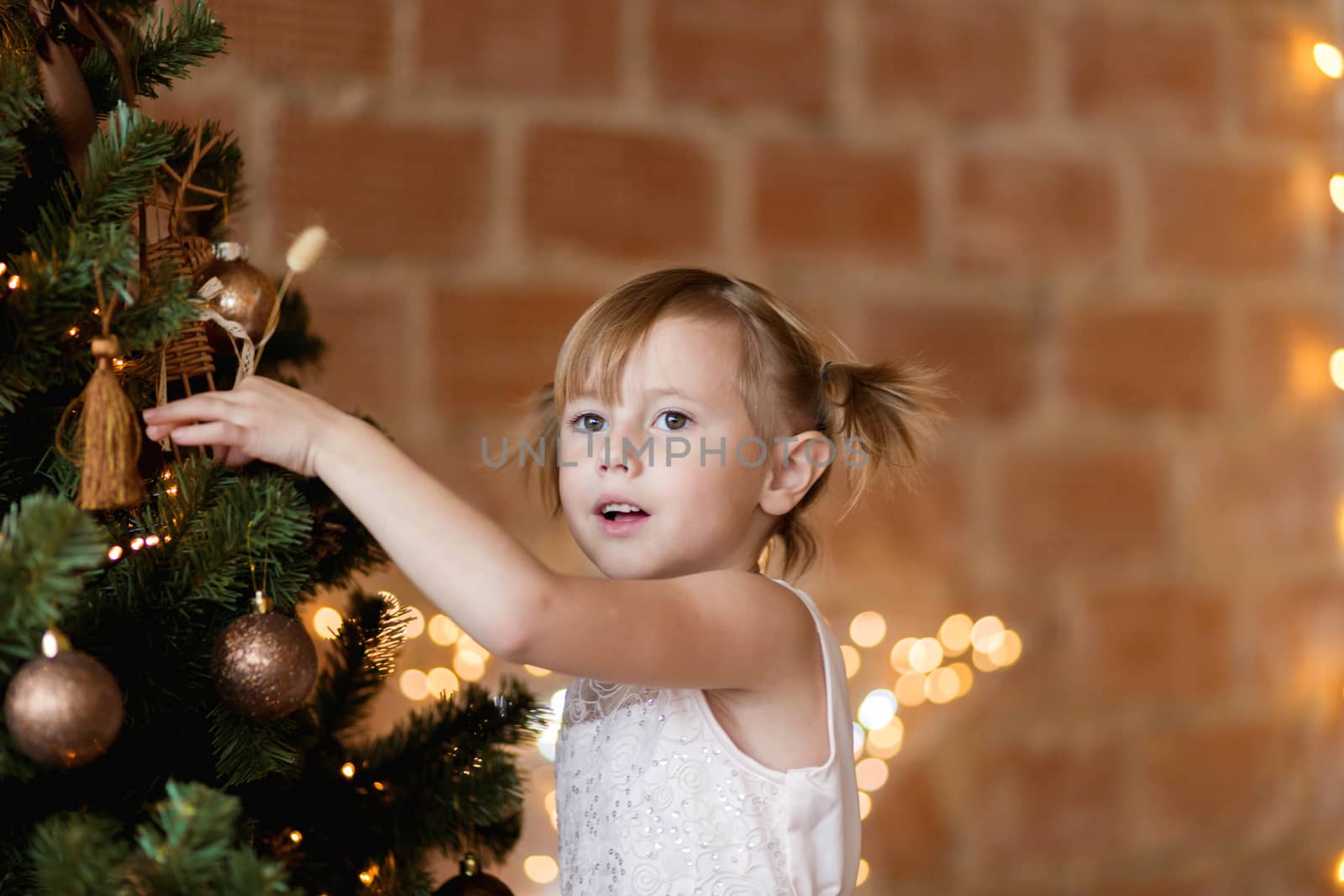 .Cute little girl in a chic dress hangs Christmas toys on the tree by galinasharapova