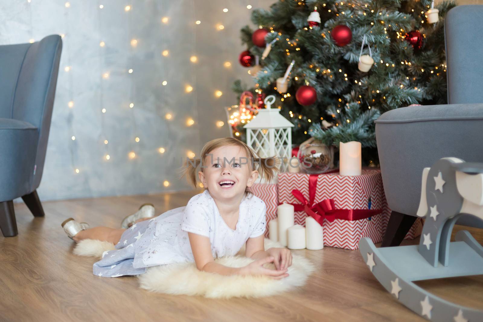 The pretty little child lies on the floor in front of Christmas tree by galinasharapova