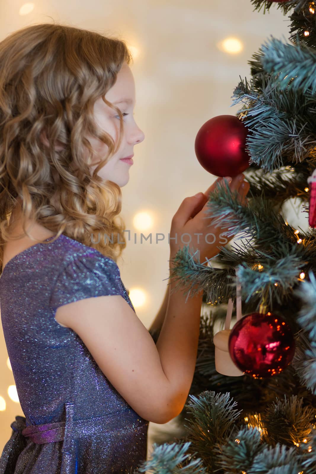 .Cute little girl in a chic dress hangs Christmas toys on the tree by galinasharapova