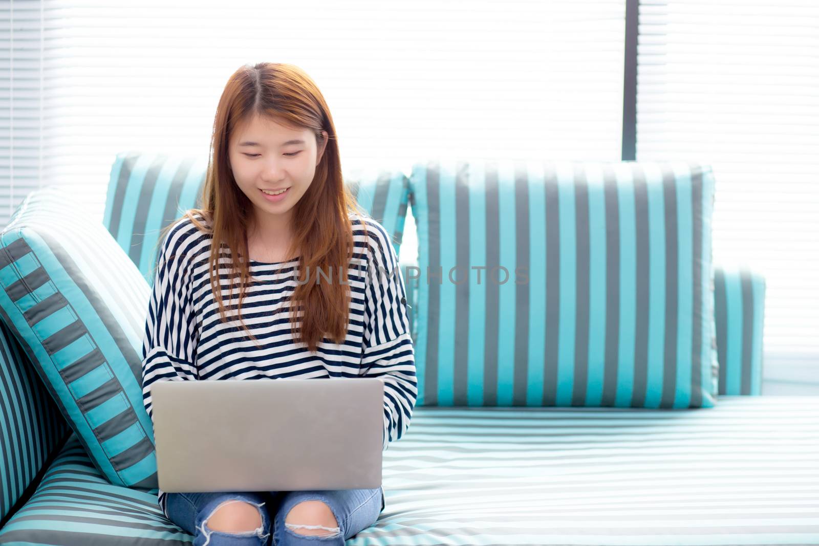 Beautiful of portrait asian young woman working online laptop sitting on sofa at living room, girl using notebook computer with connect to internet, business and success concept.
