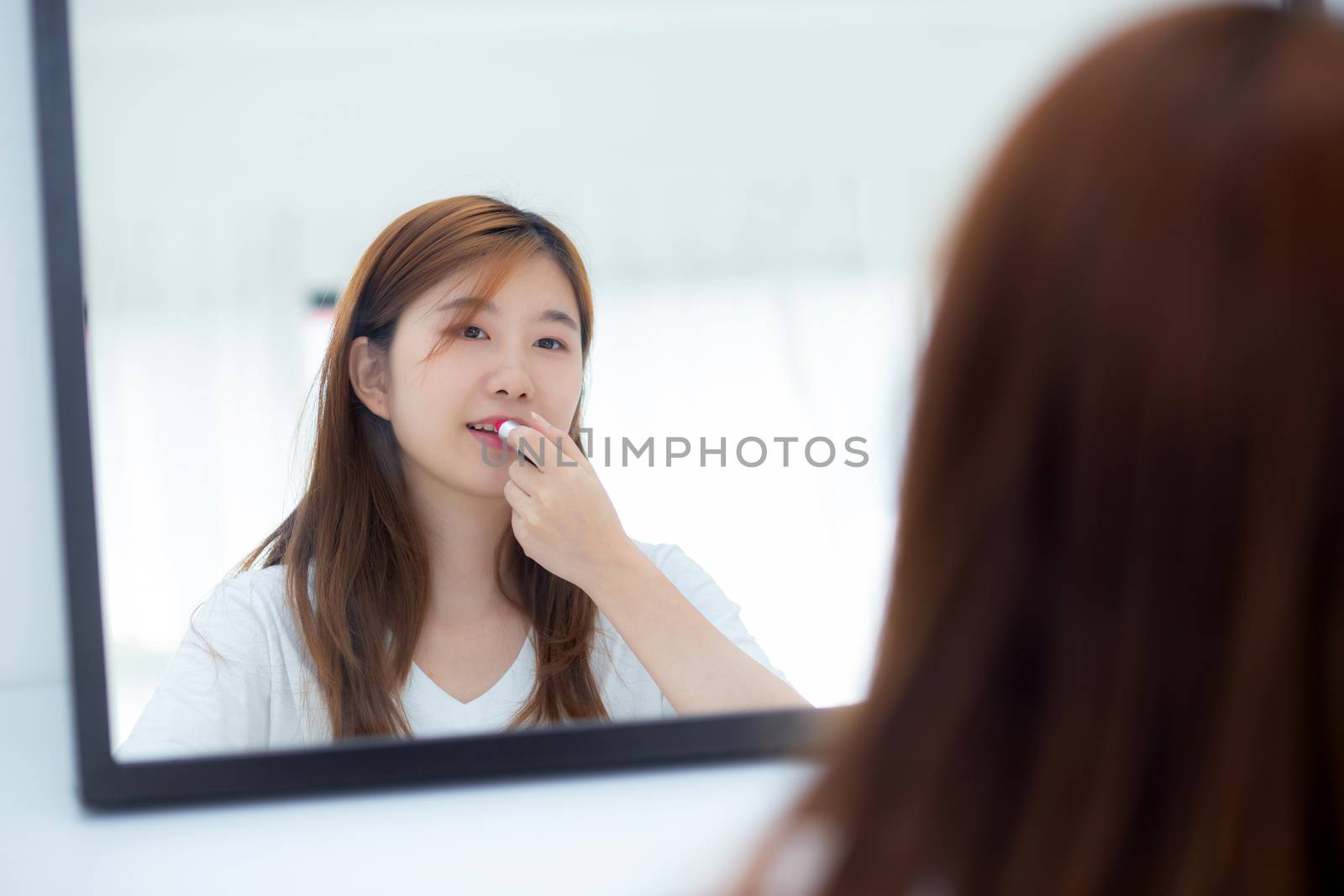 Beauty of portrait of young asian woman at the mirror holding and looking a makeup lipstick, Beautiful girl beauty fashion at the room, lifestyle concept.