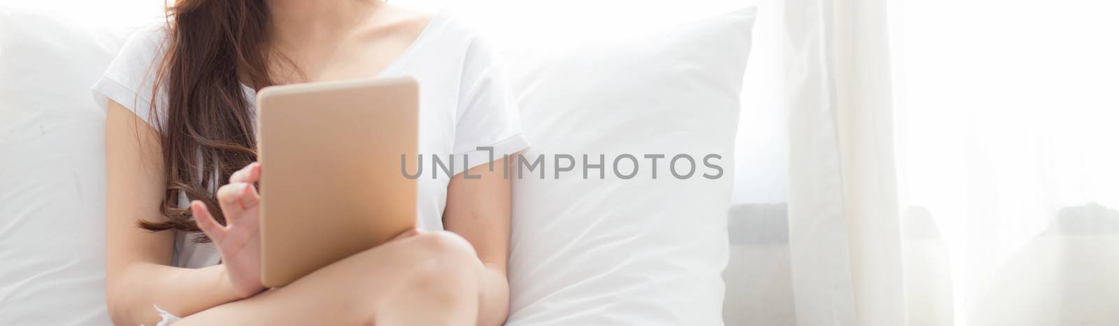 Banner website beautiful asian young woman with holding and reading digital tablet computer with leisure, girl using tablet with relax at bedroom, lifestyle and communication concept.