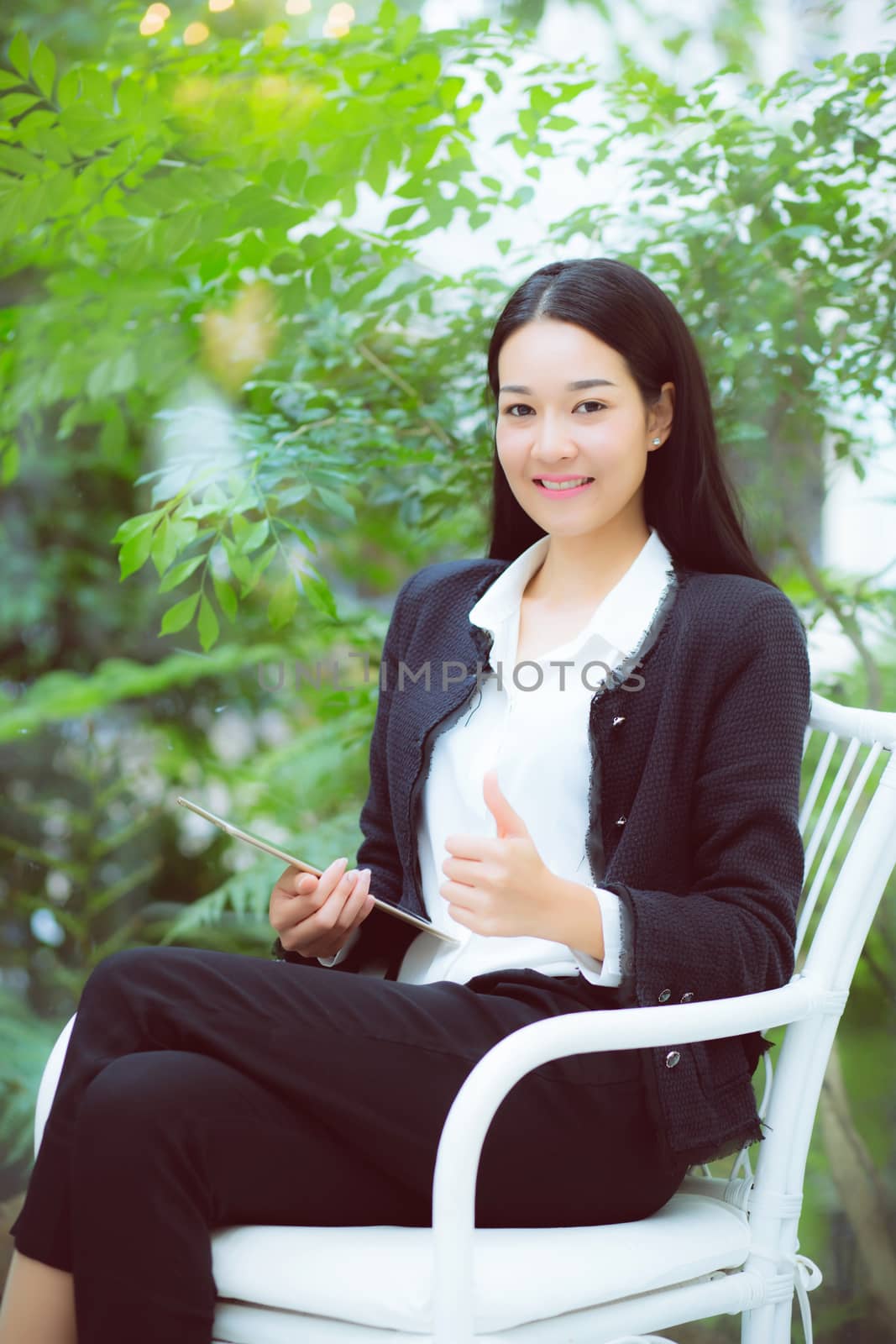 Beautiful portrait business young asian woman smile and happy sitting using digital tablet computer work at home, businesswoman on chair gesture excellent sign, communication concept.