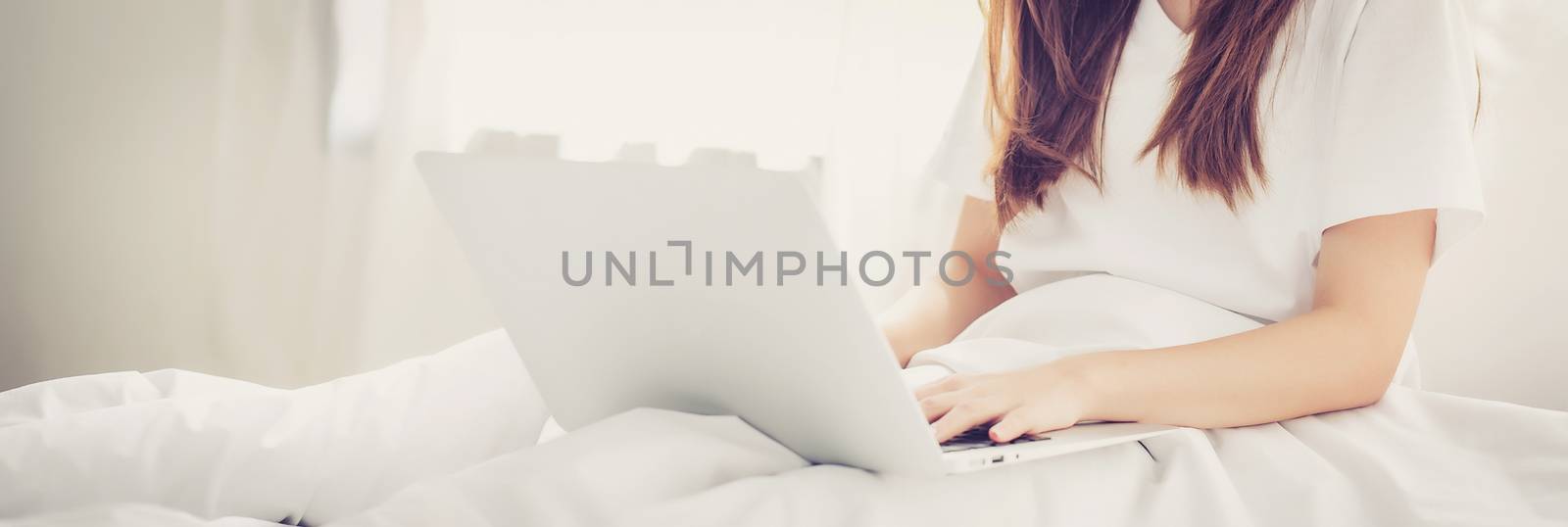 Banner website beautiful asian young woman setting on bed using laptop computer at bedroom for leisure and relax, freelance with girl working notebook, communication and lifestyle concept.