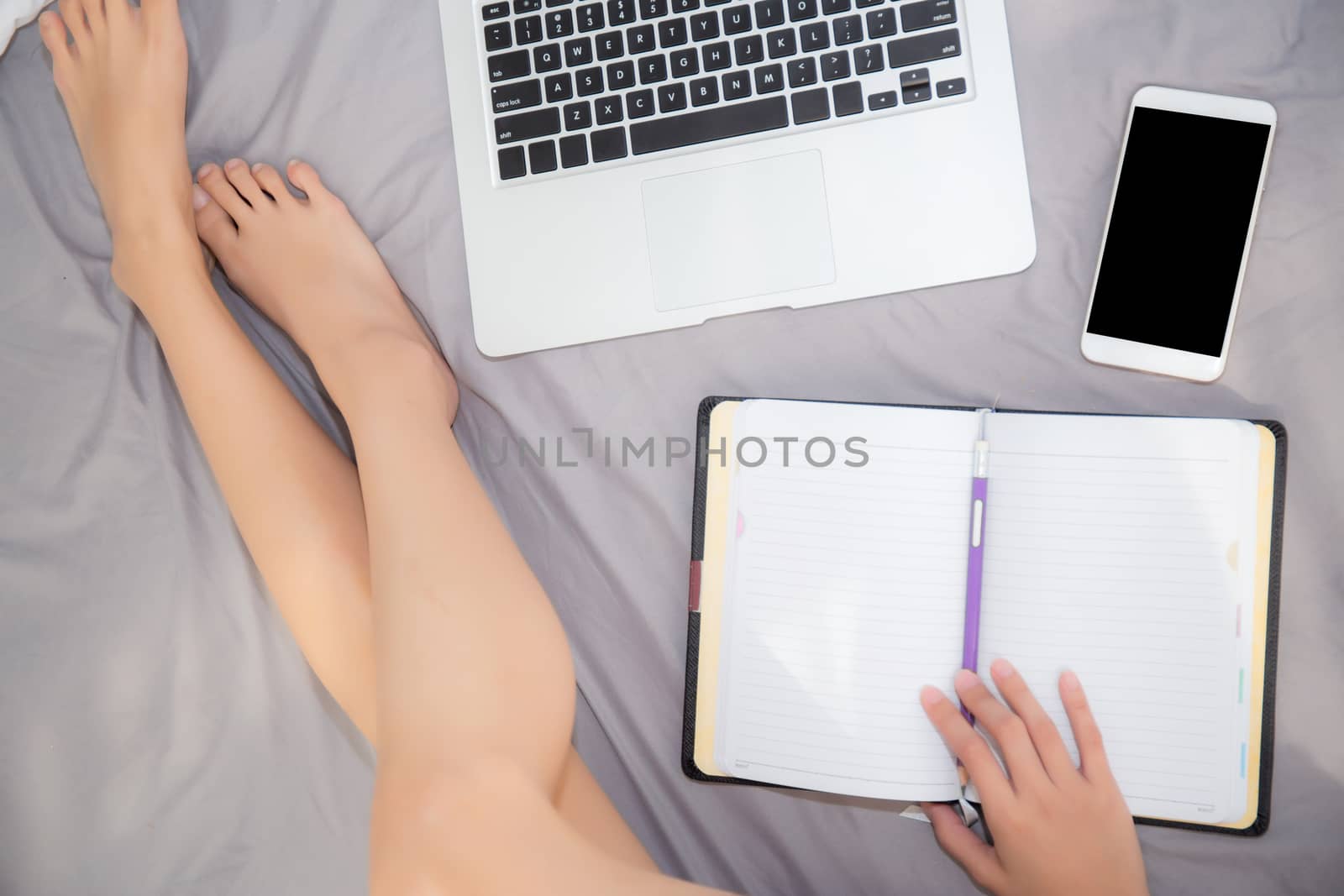 Top view woman legs with work on notebook, laptop and smart mobile phone, girl relax and resting on bed at the bedroom, communication and freelance concept