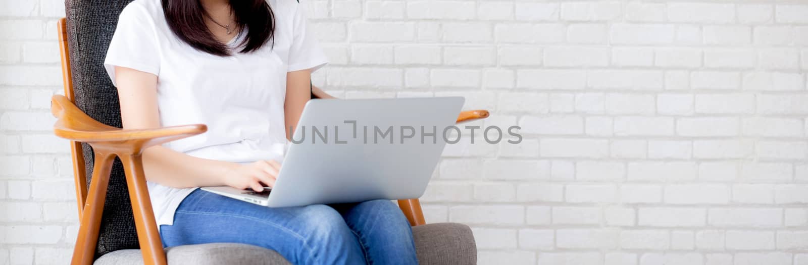 Banner website beautiful asian young woman working online laptop sitting on chair on cement brick white background, girl using notebook computer, business concept.