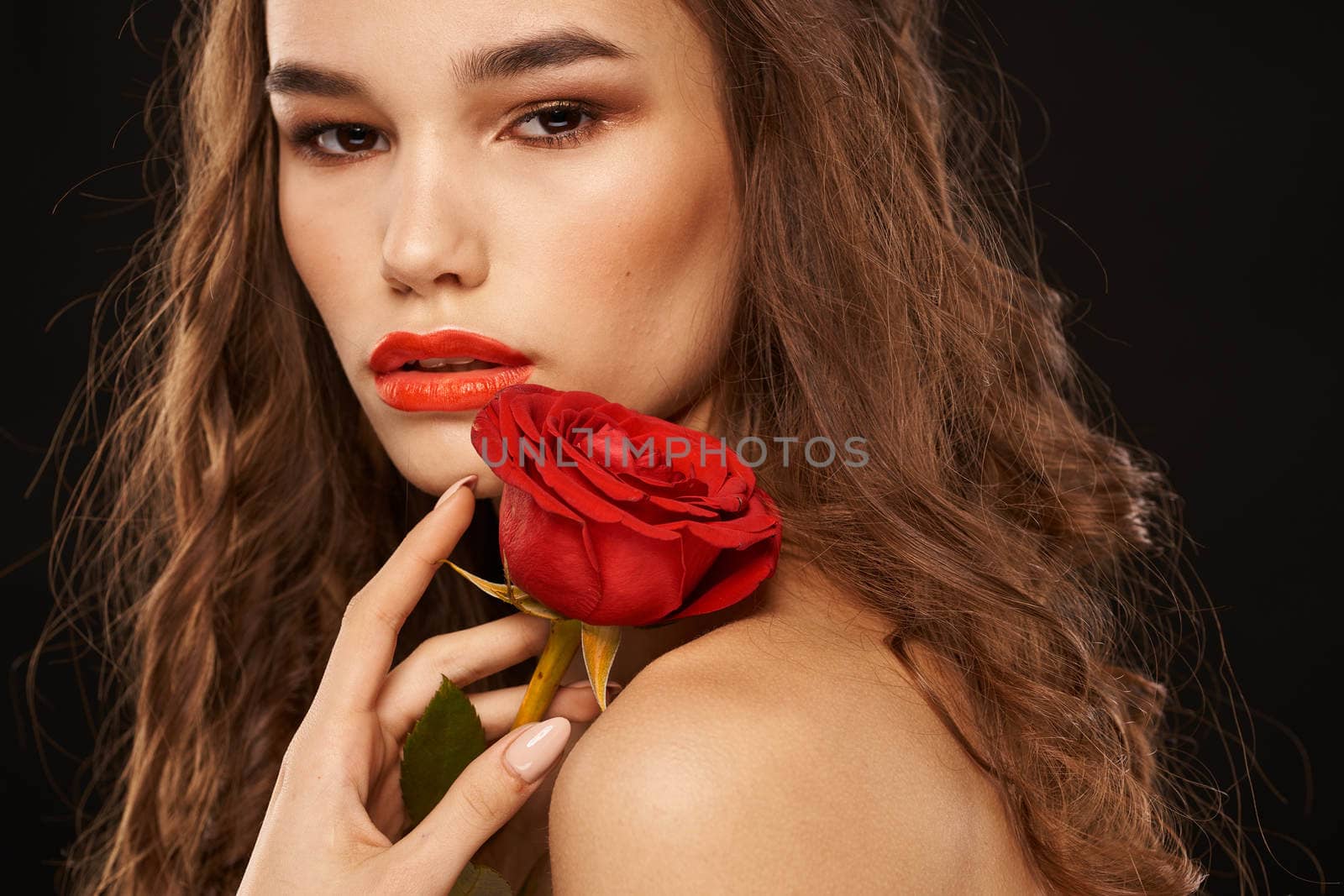 woman with a red rose on a dark background long hair makeup red lips. High quality photo