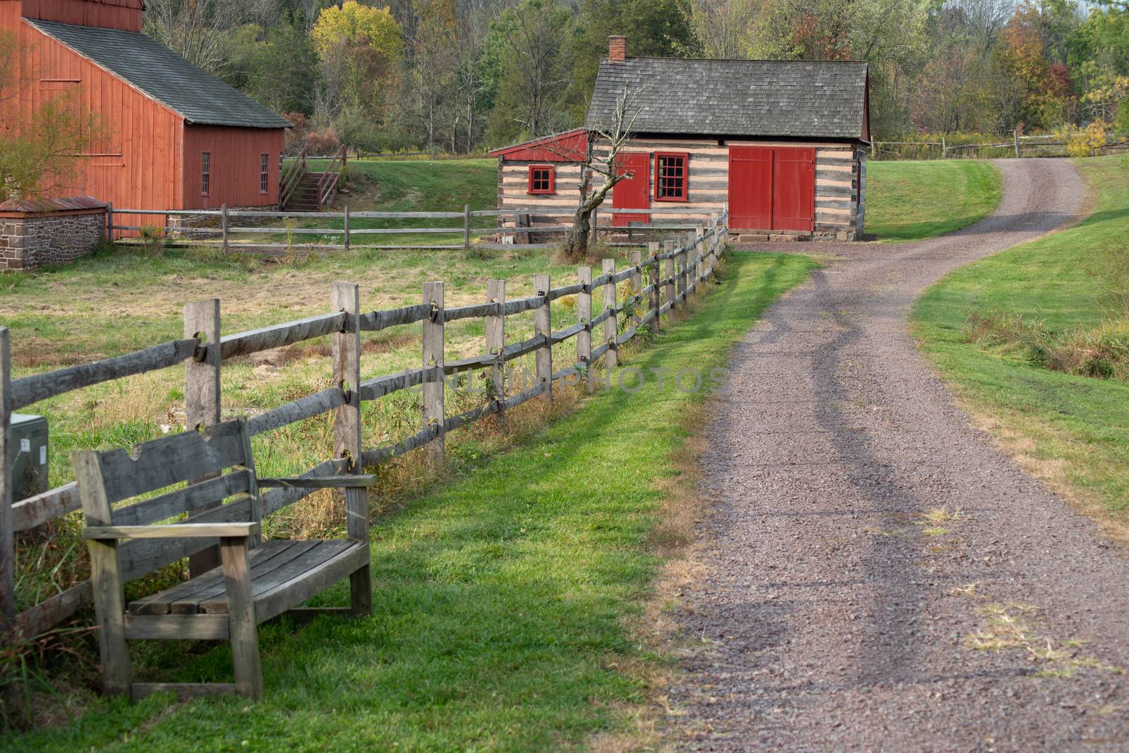Gravel path leads past an empty bench, red barn and log cabin by marysalen