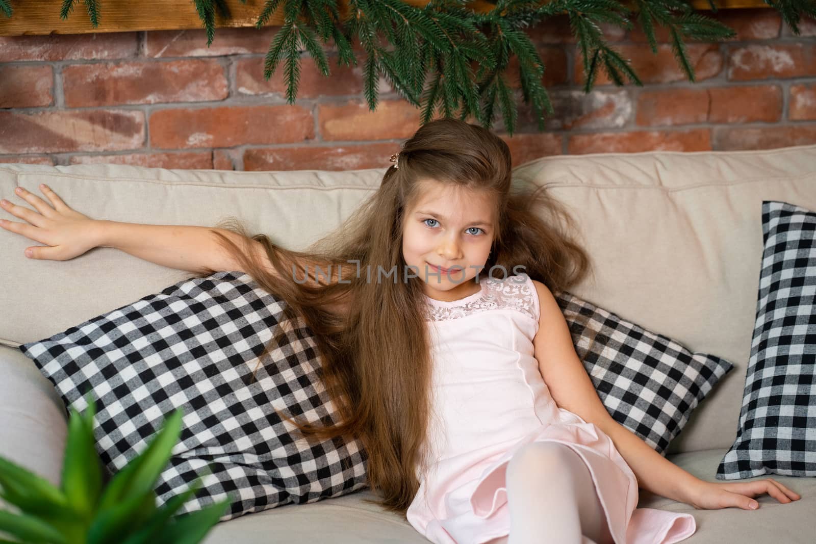 A little girl is sitting on a cozy sofa with checkered pillows.