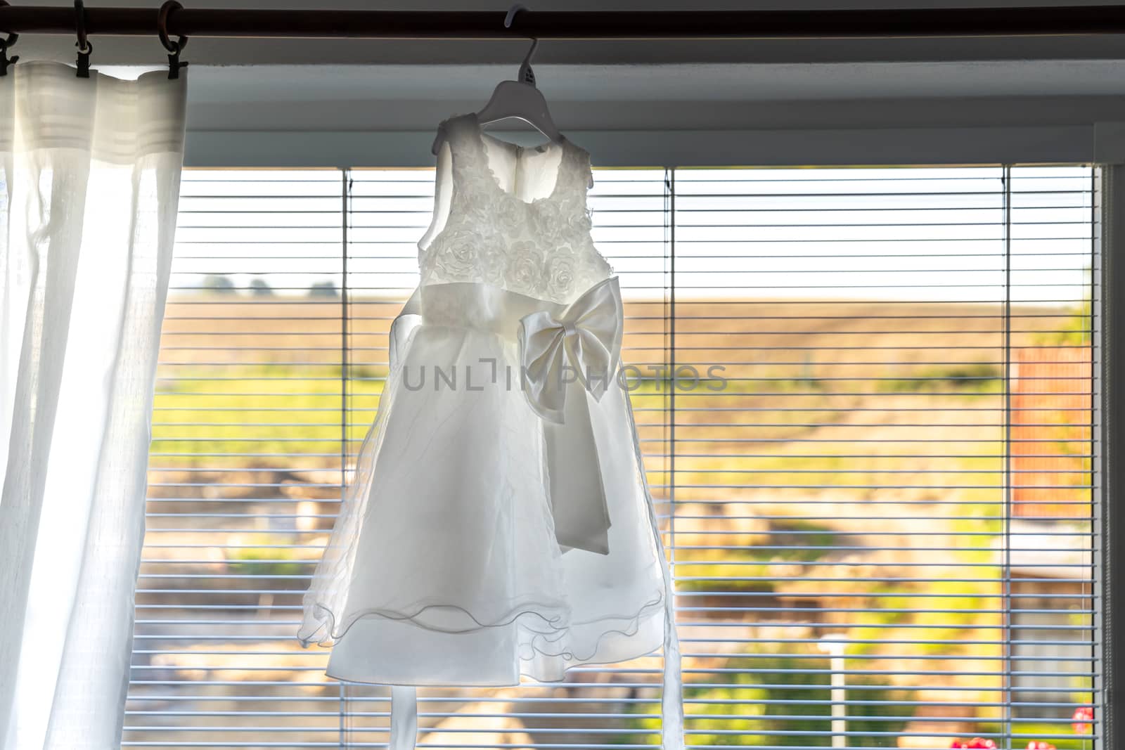 children wedding dress hanging on window cornices by Edophoto