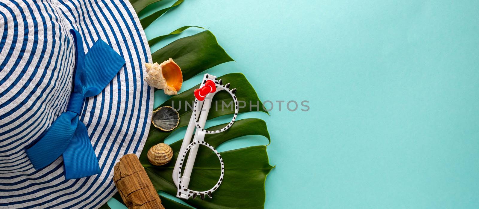 Striped hat, sunglasses, seashells, tropical monstera leaves on a blue background.
