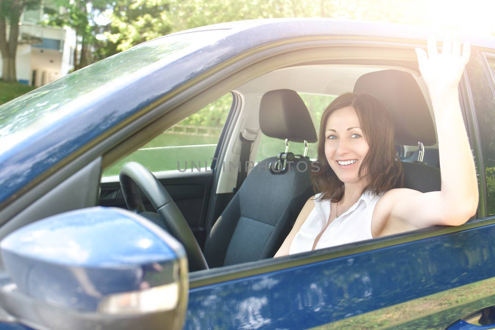 say hello, Beautiful happy adult woman sits in the car and waving his hand in greeting