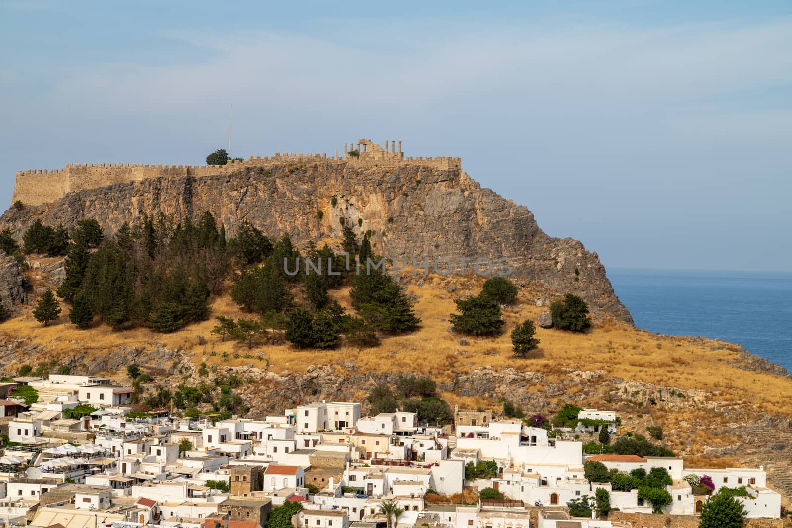 Scenic view at the city of Lindos with white houses, the antique Acropolis on top of the mountain and a bay on Rhodes island, Greece on a sunny day in spring