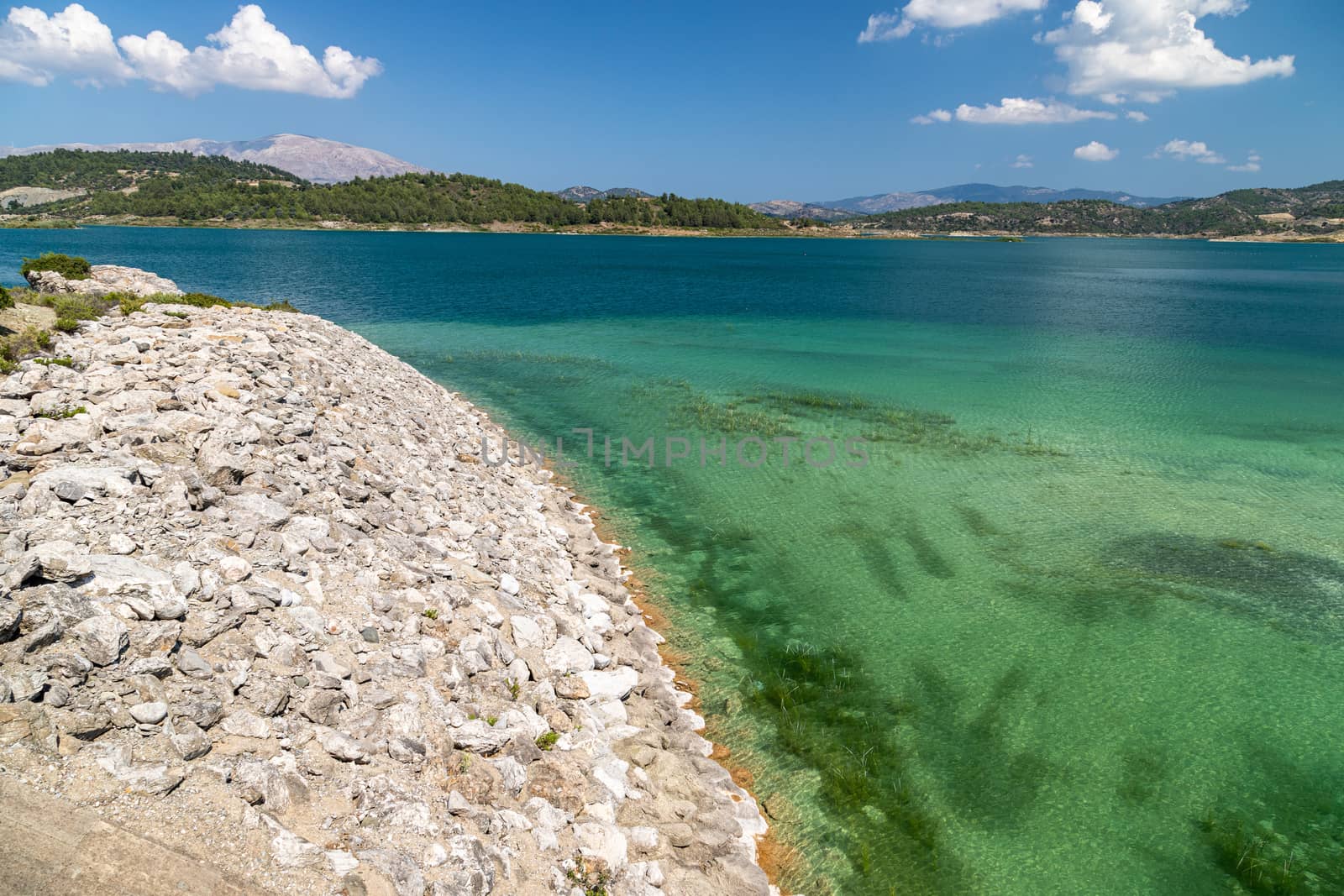 Scenic view at the Gadoura water reservoir on Rhodes island, Greece with stony shore, blue and turquoise water and landscape in background