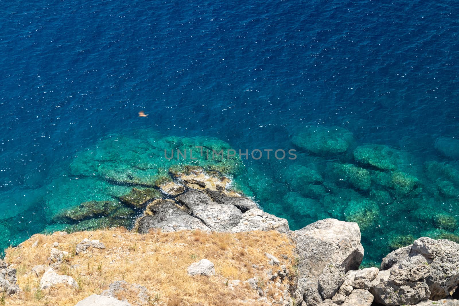 View from the acropolis on the rocky coast with blue and turquoise water in Lindos on Rhodes island, Greece on a sunny day in spring