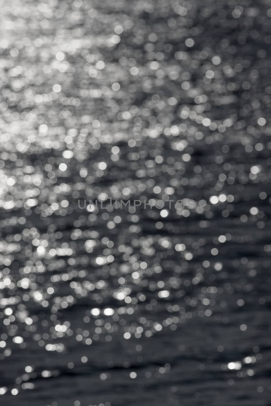 5 - Defocused vertical image of sunny water ripples, forming an abstract textured plain background of random white bokeh circles. Water theme.