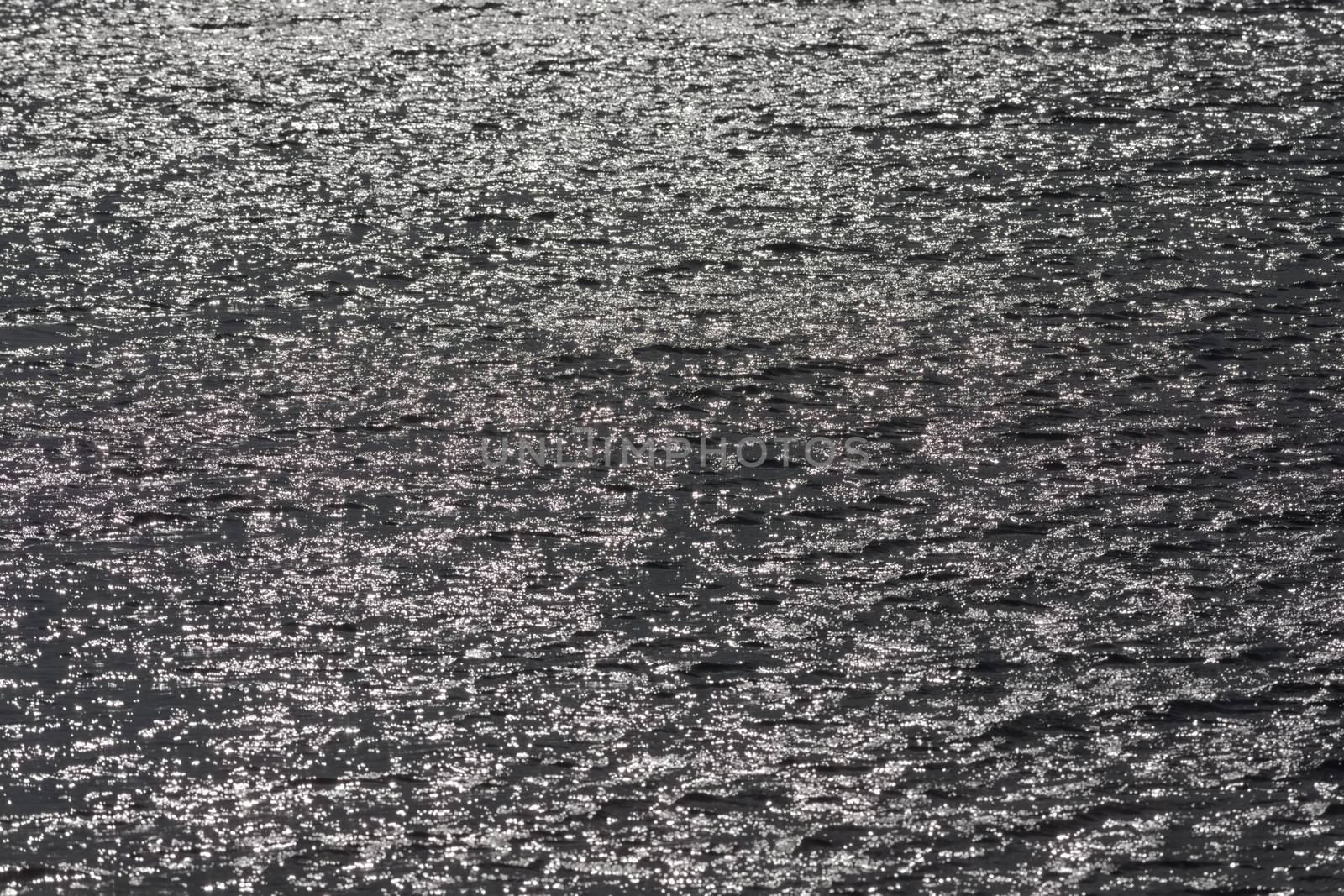 1 - Full frame sunlight shining off surface ripples of large reservoir lake. Glittery shimmer effect. monochrome grey with bright sun flare spots.