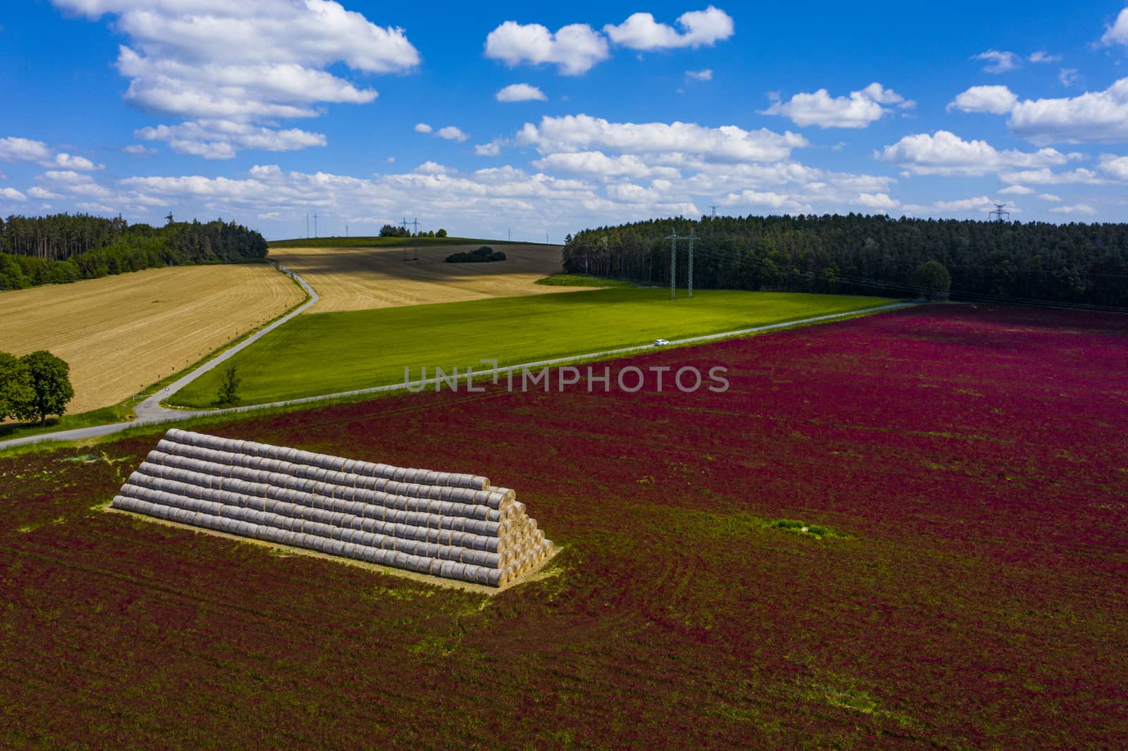 Red blooming crimson clover field (Trifolium incarnatum) and heap of hay bales seen from above