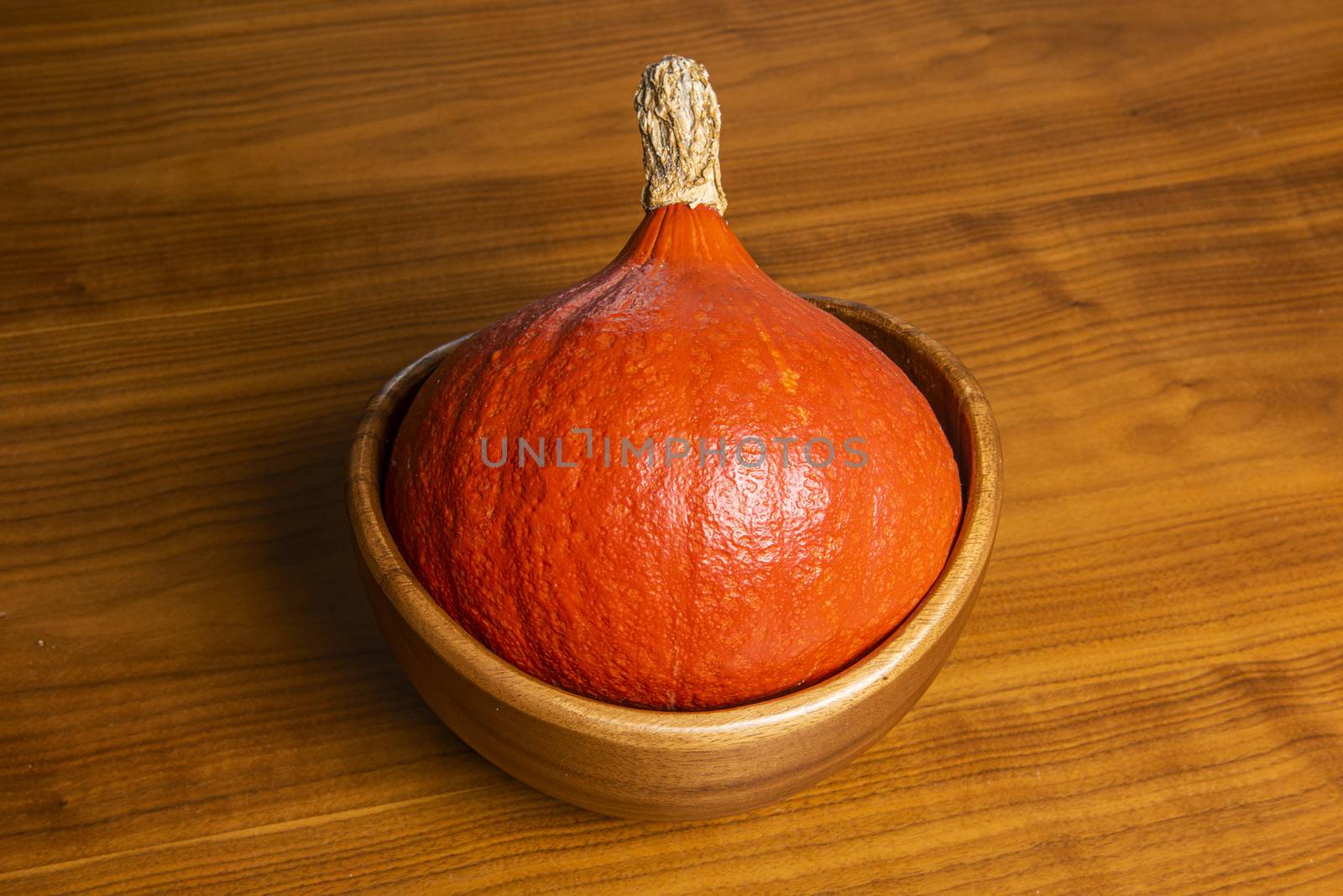 Orange pumpkin lying in a wooden bowl on a table