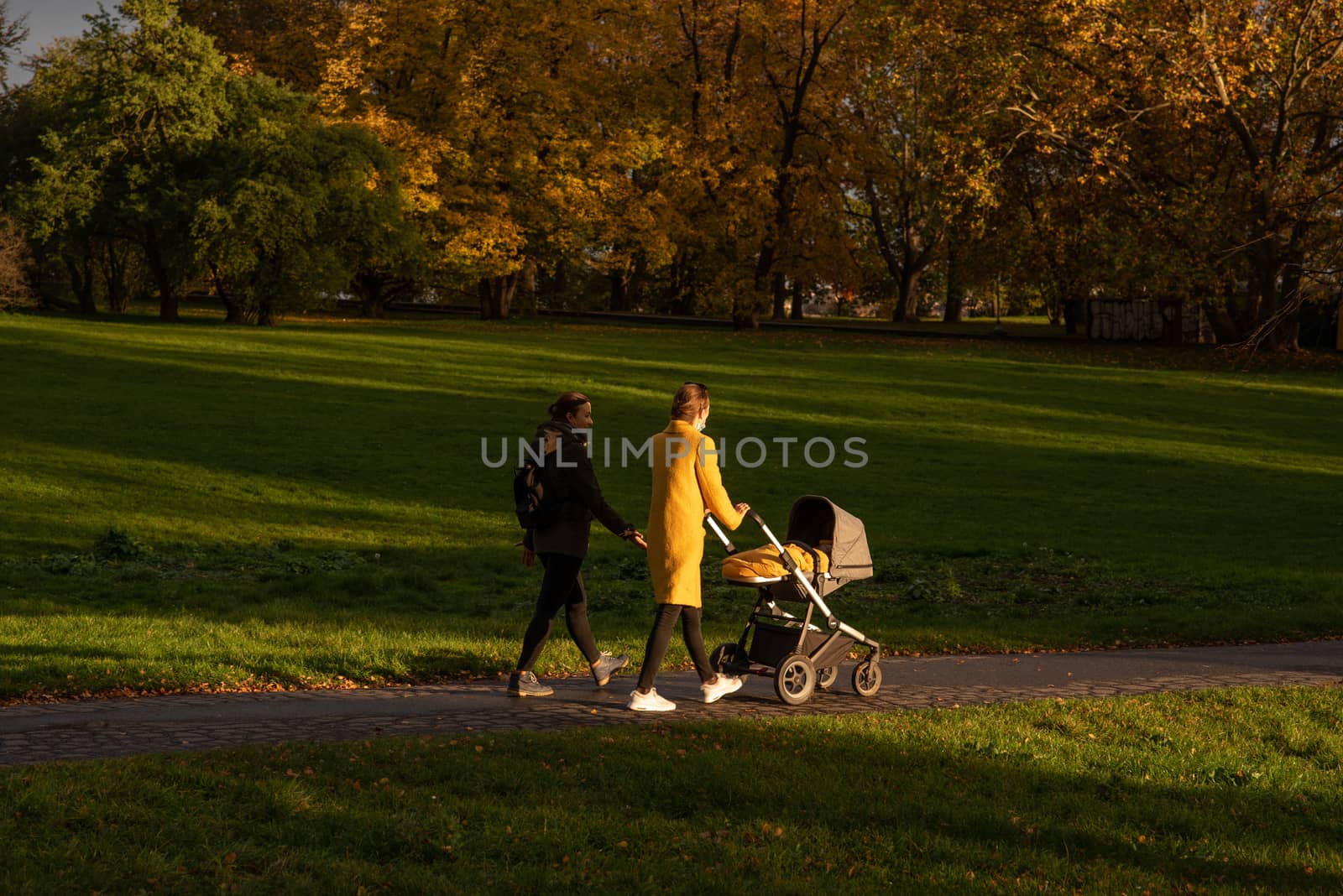 Two friends walking on the park while one is carrying a stroller with a baby in Prague, Czech republic