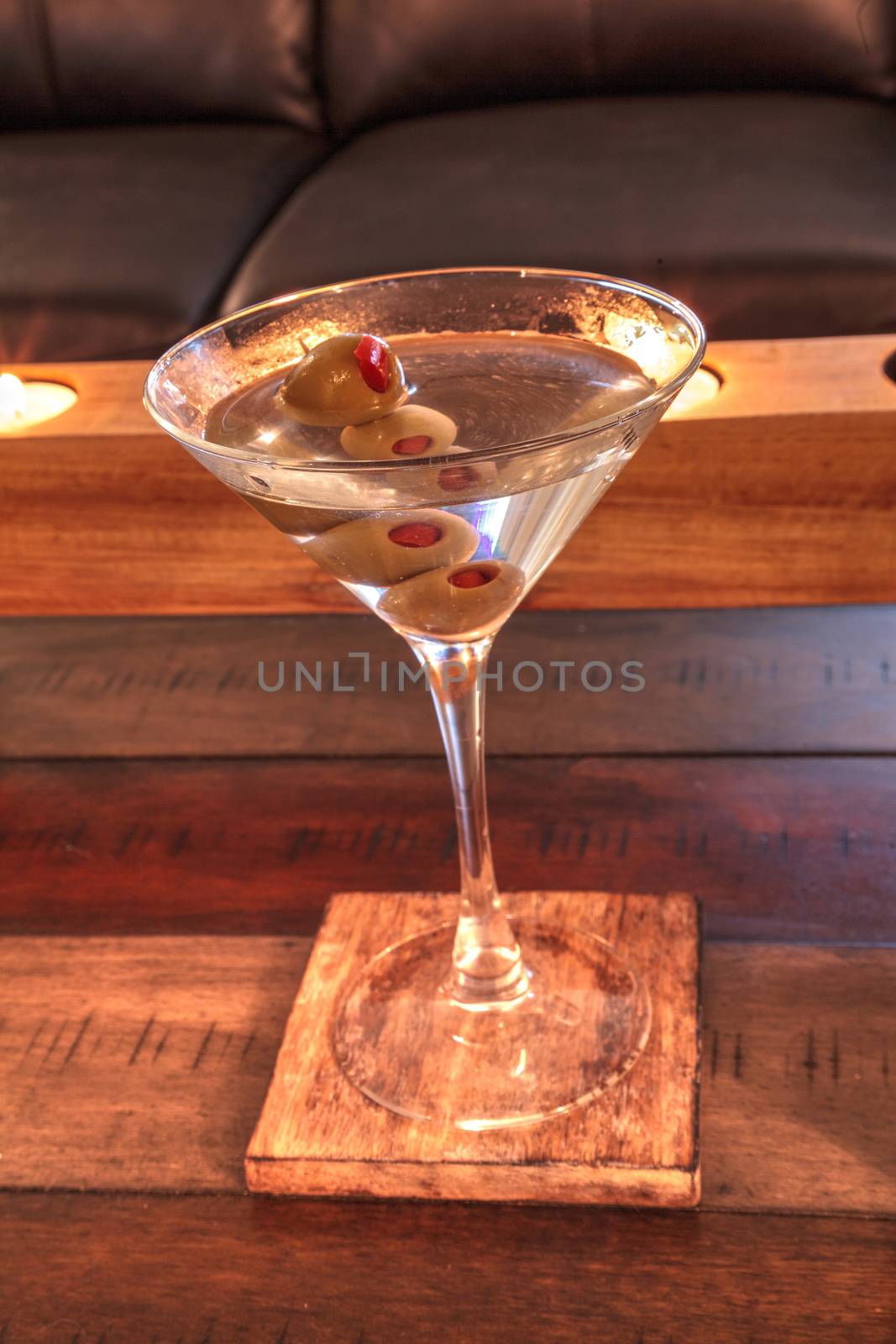 Dirty martini with green Pimento olive on a rustic wood coaster by steffstarr