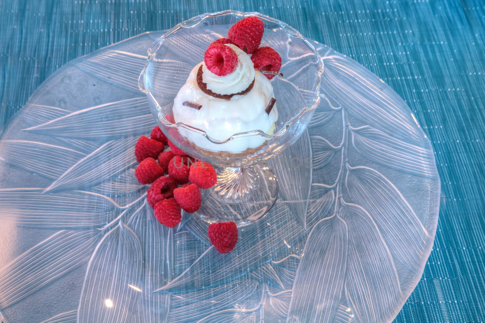 Dessert dish of cheesecake, shaved chocolate and raspberries on a glass plate.