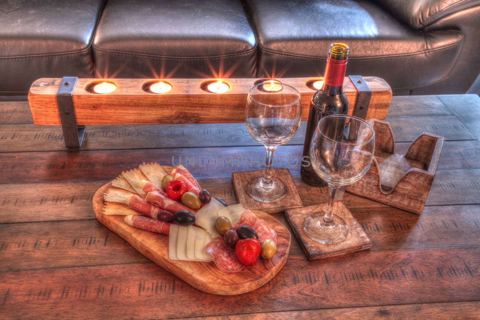 Red wine with Charcuterie board on rustic wood with candles behind a spread of prosciutto panino, mozzarella cheese, Genoa salami, Fontina cheese and artisanal crackers.