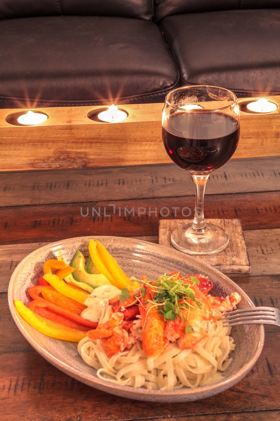Red wine with Maine lobster over a bed of linguini with micro greens, colorful peppers and avocado sauce.
