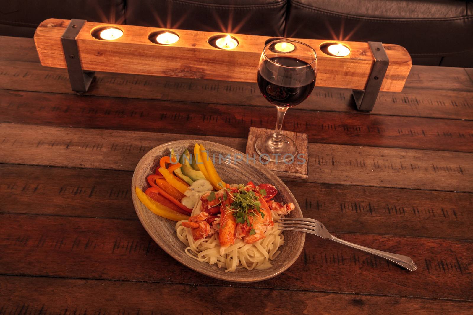 Red wine with Maine lobster over a bed of linguini with micro greens, colorful peppers and avocado sauce.